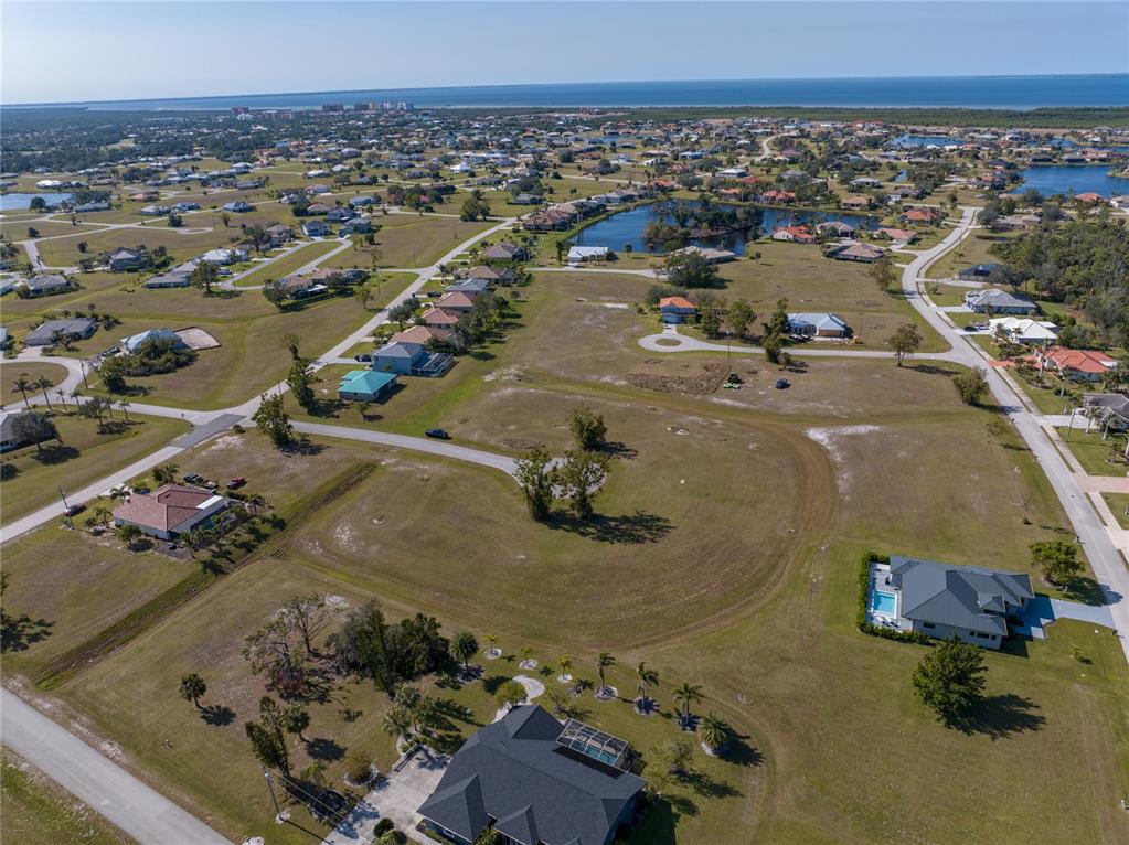 An aerial view shows a residential neighborhood with scattered houses, vacant lots, and a pond — 17154 SUGAR COURT, PUNTA GORDA, FL
