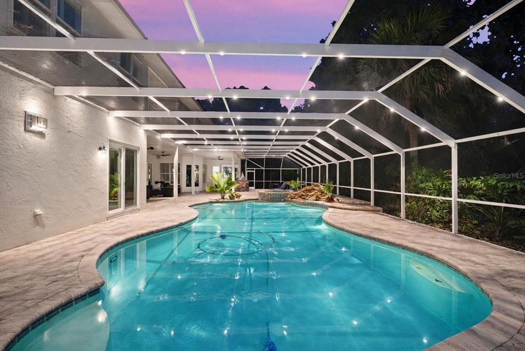 A screened-in swimming pool with a rock water feature sits on a stone patio — 6413 MACLAURIN DRIVE, TAMPA, FL