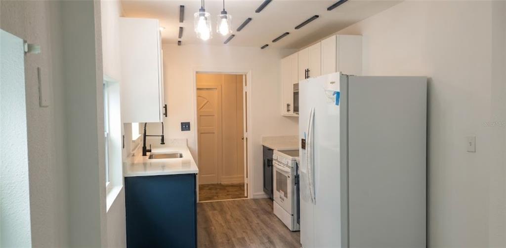A kitchen features white upper cabinets, dark blue lower cabinets, and a white refrigerator — 1412 LAUREL STREET, PALATKA, FL