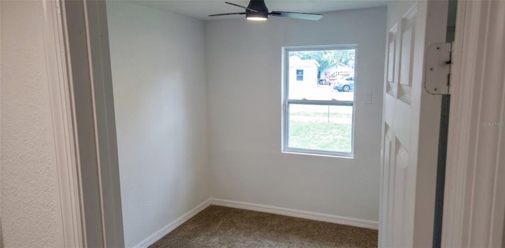 A small, empty room features light-colored walls, brown carpeting, a ceiling fan, and a window — 1412 LAUREL STREET, PALATKA, FL