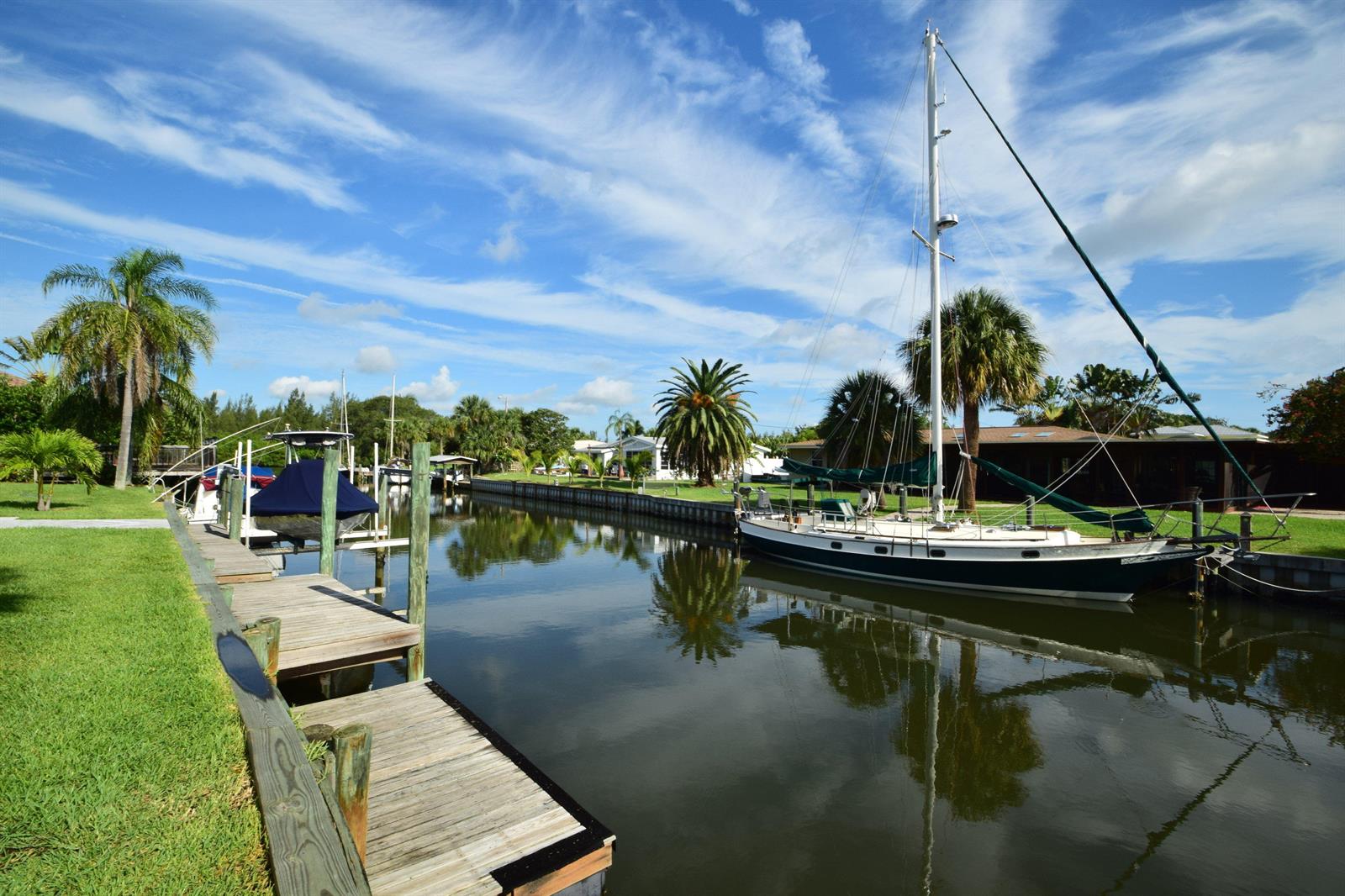 A sailboat is docked in a canal next to a wooden pier and palm trees — 705 Bahia Mar Road, FL, FL