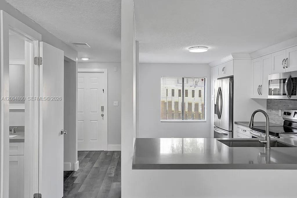 A kitchen with white cabinets and a gray countertop overlooks a hallway and entryway — 5084 S University Dr, Davie FL 33328, DAVIE, FL