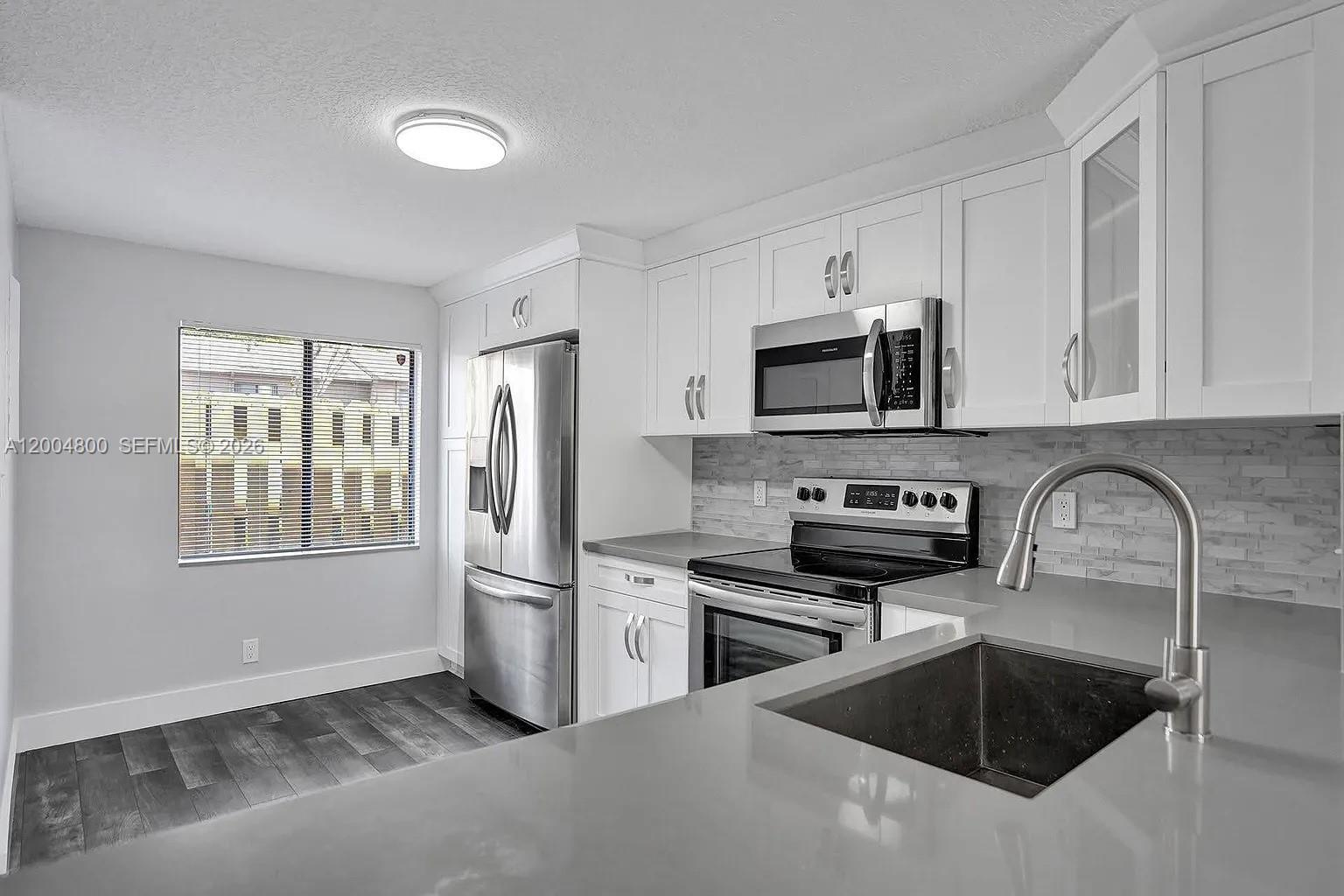 A modern kitchen features white cabinets, stainless steel appliances, gray countertops, and wood-look flooring — 5084 S University Dr, Davie FL 33328, DAVIE, FL
