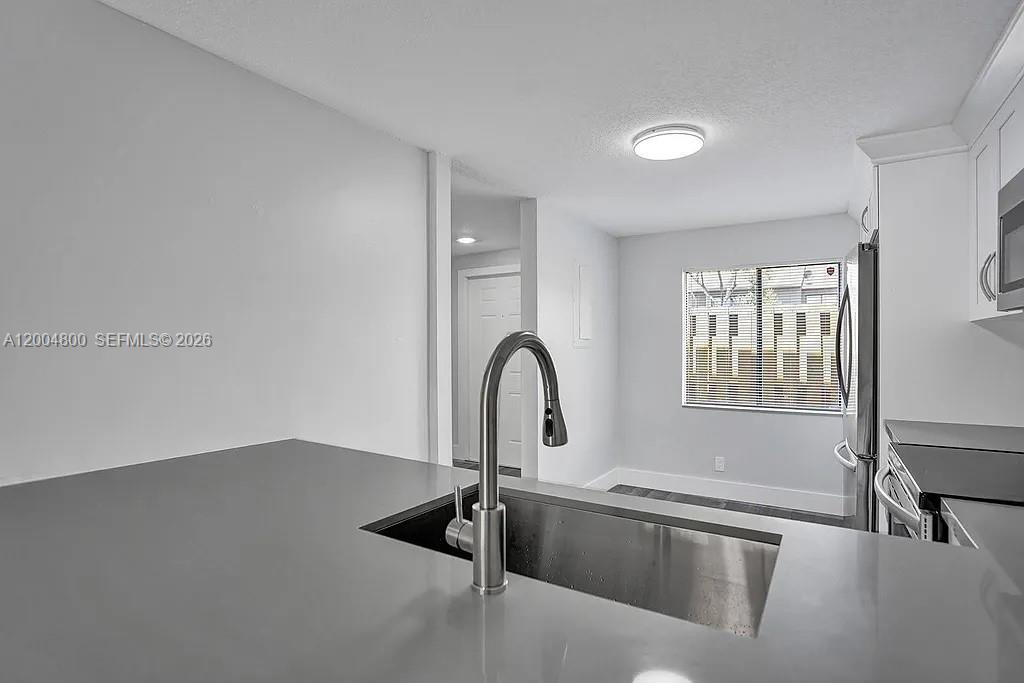 A modern kitchen features a stainless steel sink, gray countertops, and white cabinetry — 5084 S University Dr, Davie FL 33328, DAVIE, FL