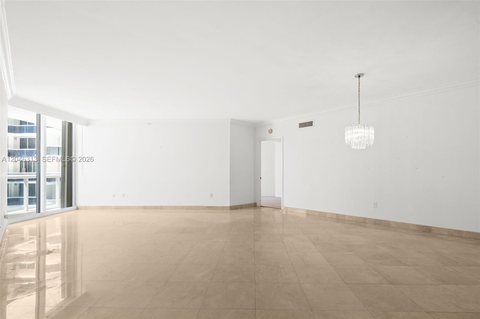 An empty living room features white walls, beige tile flooring, and a crystal chandelier — 9595 Collins Ave # D, Surfside FL 33154, SURFSIDE, FL