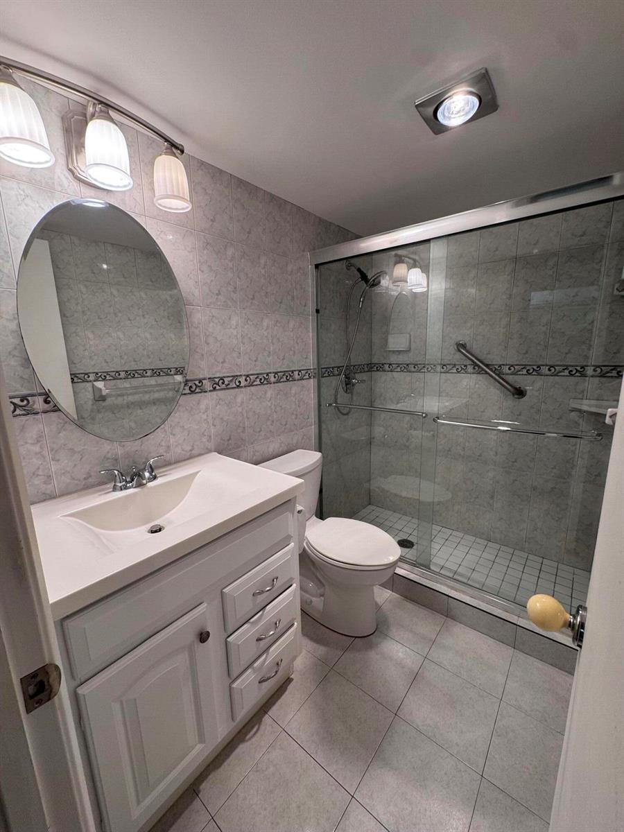 A bathroom features a white vanity, an oval mirror, a toilet, and a glass-enclosed shower — 5660 SW 3rd Place # 105, Margate FL 33068, MARGATE, FL
