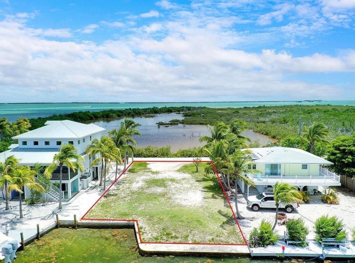 An aerial view shows a vacant waterfront lot situated between two elevated residential houses — 28525 Jolly Roger Drive, FL 33042, FL