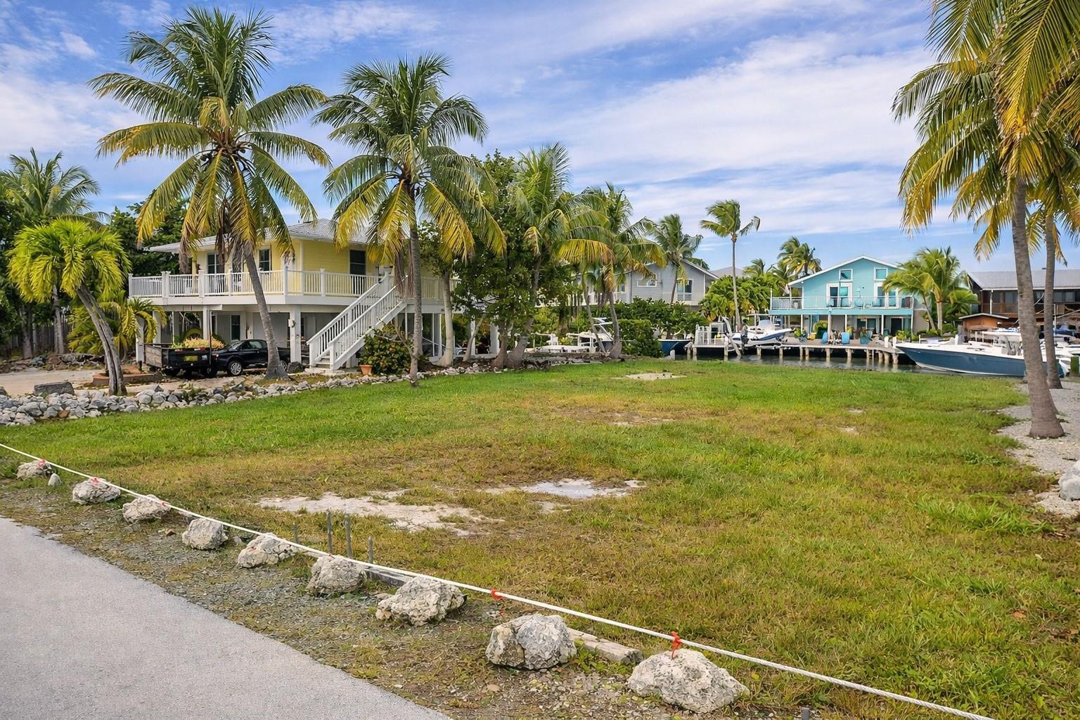 A vacant grassy lot sits between two elevated houses with palm trees and a boat dock — 28525 Jolly Roger Drive, FL 33042, FL