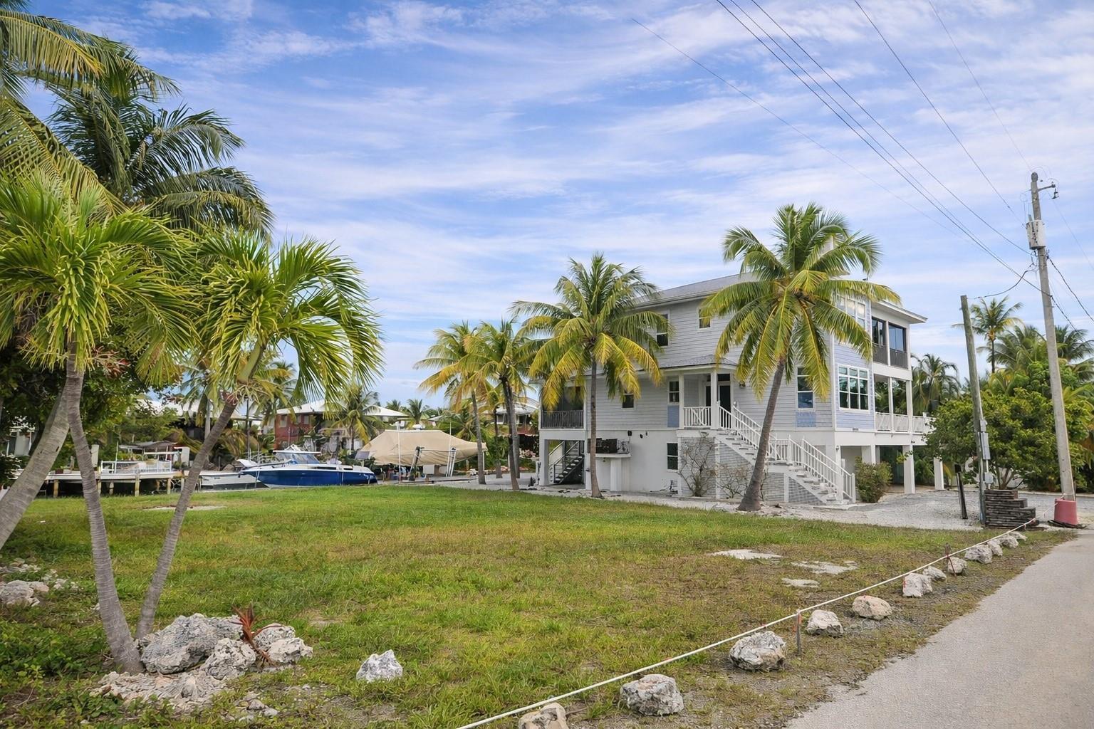 A light blue elevated house stands on a grassy lot with palm trees and boats — 28525 Jolly Roger Drive, FL 33042, FL