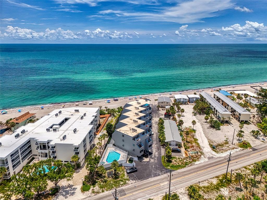 An aerial view shows beachfront apartment buildings, a swimming pool, and a coastal road — 2400 N BEACH ROAD UNIT 17, ENGLEWOOD, FL