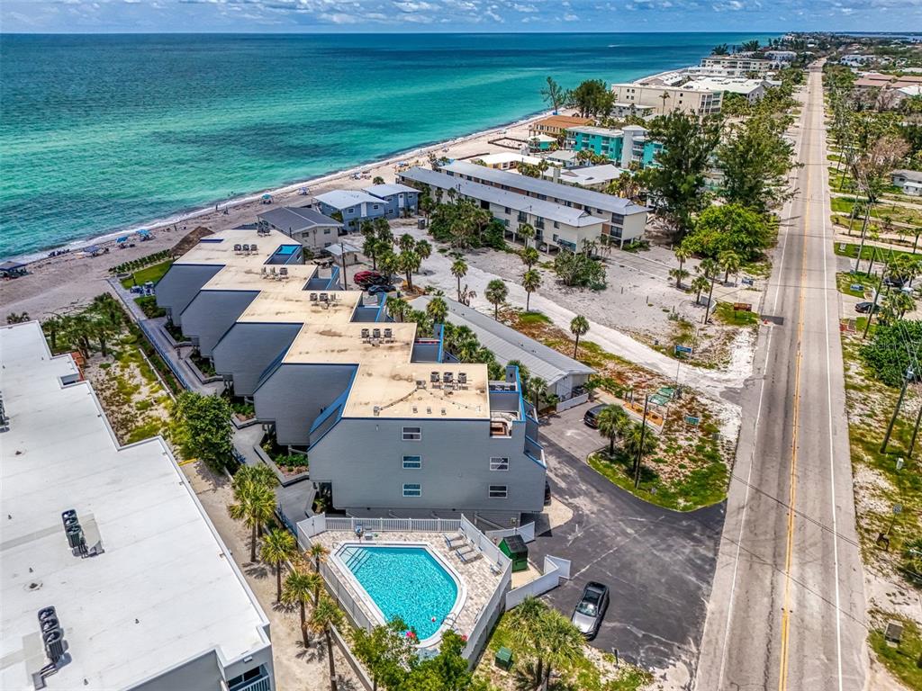 An aerial view shows a multi-story beachfront condominium complex with a swimming pool and road — 2400 N BEACH ROAD UNIT 17, ENGLEWOOD, FL