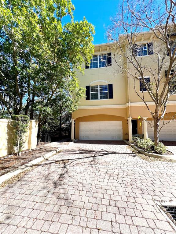 A three-story townhouse with a beige exterior and a paved driveway leading to a garage — 809 HARBOR OAK LANE, CLEARWATER, FL