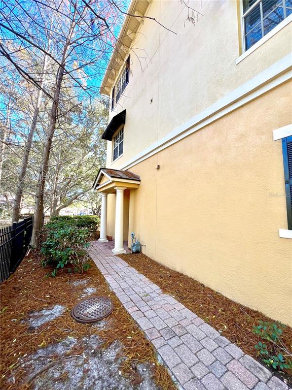 A side view of a tan stucco building with a brick walkway and covered entrance — 809 HARBOR OAK LANE, CLEARWATER, FL