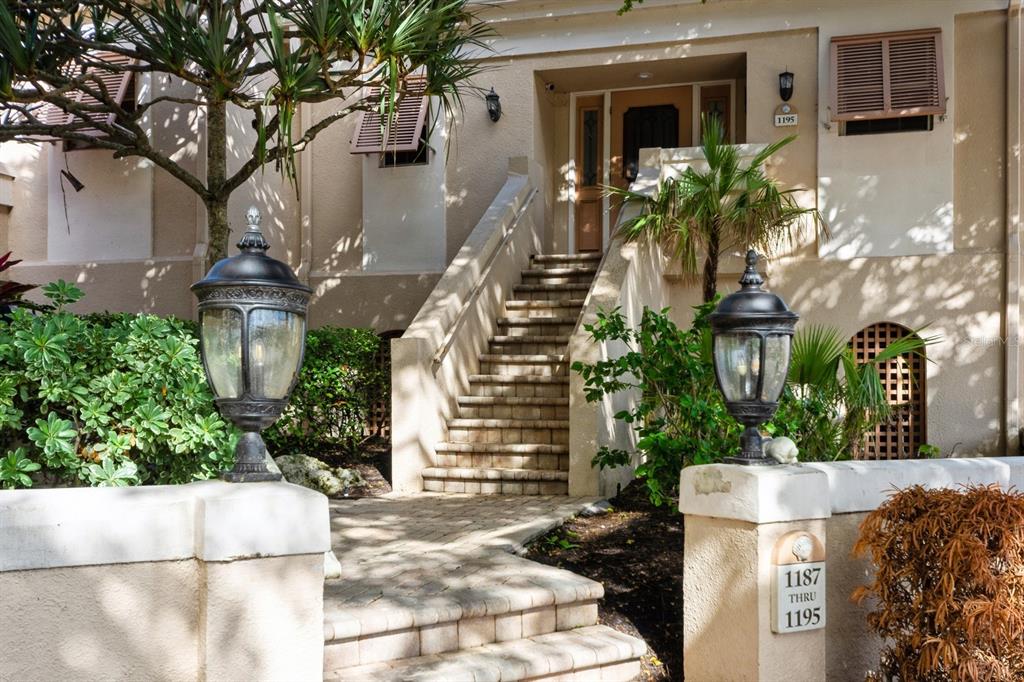 A stone staircase leads to the entrance of a tan building with two outdoor lamps — 1195 COQUILLE STREET UNIT 309, SARASOTA, FL