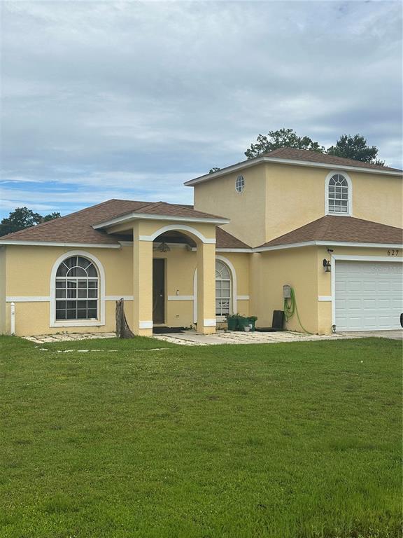 A yellow two-story house with a brown shingled roof and a white garage door — 627 CAMEL LANE, POINCIANA, FL