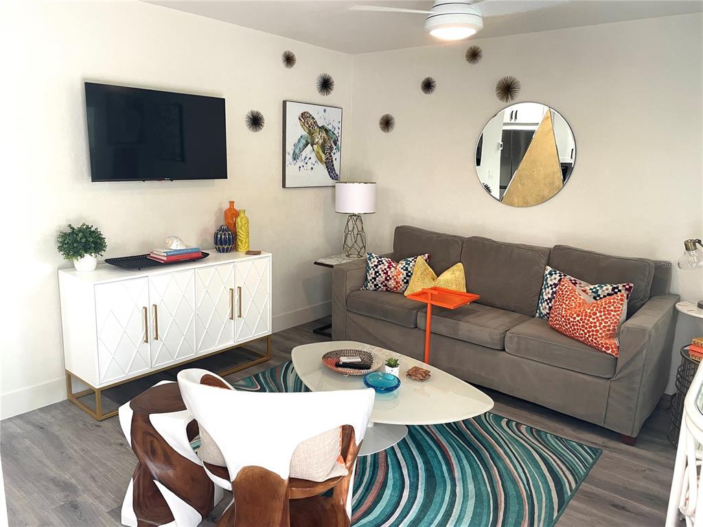 A living room features a grey sofa, white media console, patterned rug, and wall art — 1912 MORRILL UNIT 1916, SARASOTA, FL