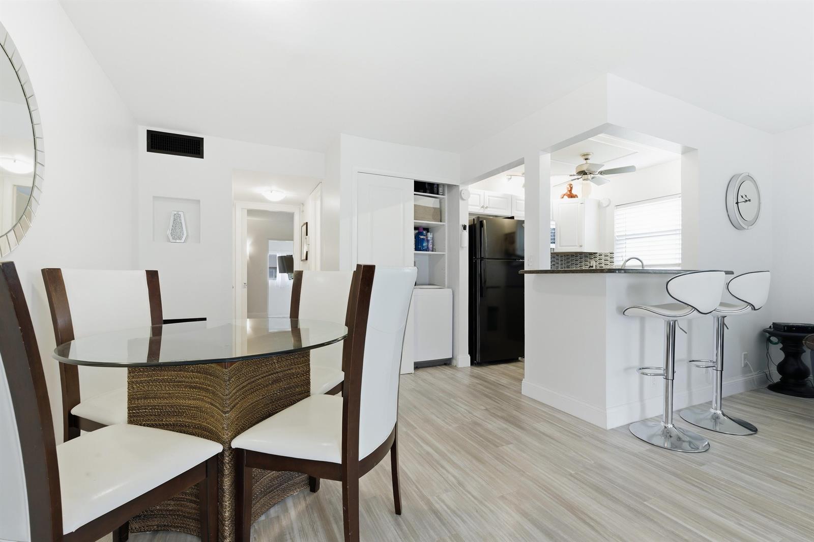 A dining area with a glass table and white chairs next to a kitchen counter — 70 Bedford # C, West Palm Beach FL 33417, WEST PALM BEACH, FL
