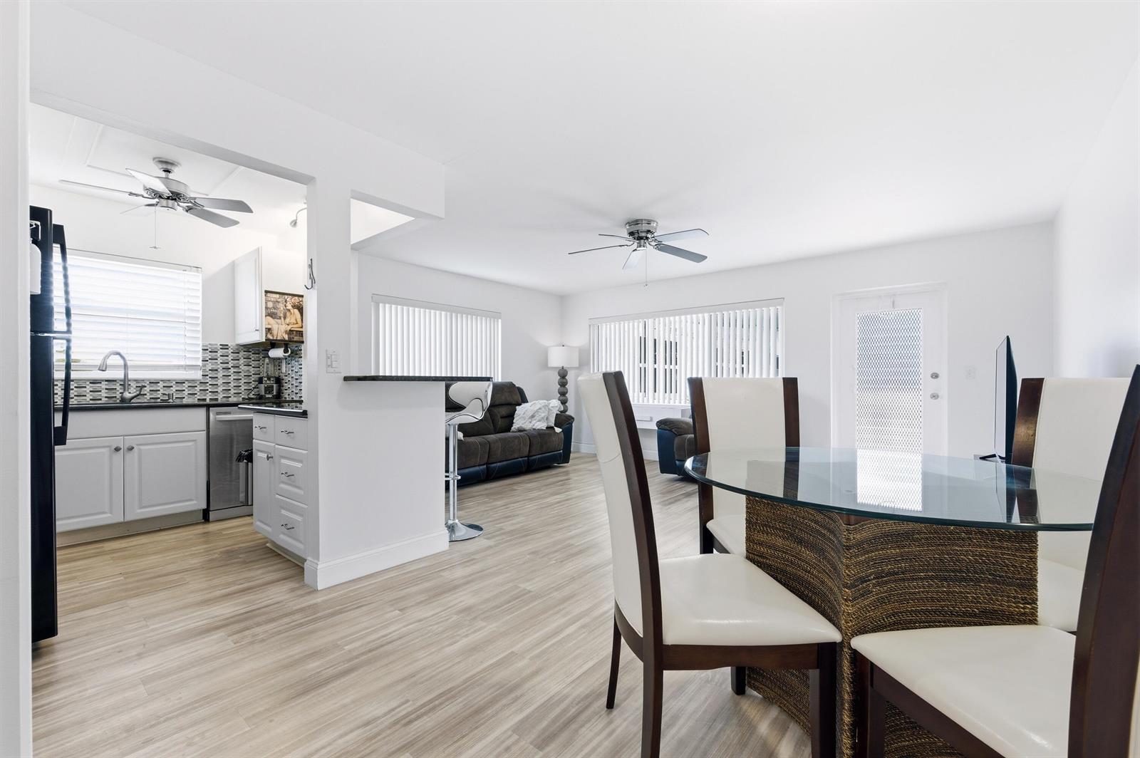A bright, open-concept living and dining area features light wood flooring and white walls — 70 Bedford # C, West Palm Beach FL 33417, WEST PALM BEACH, FL