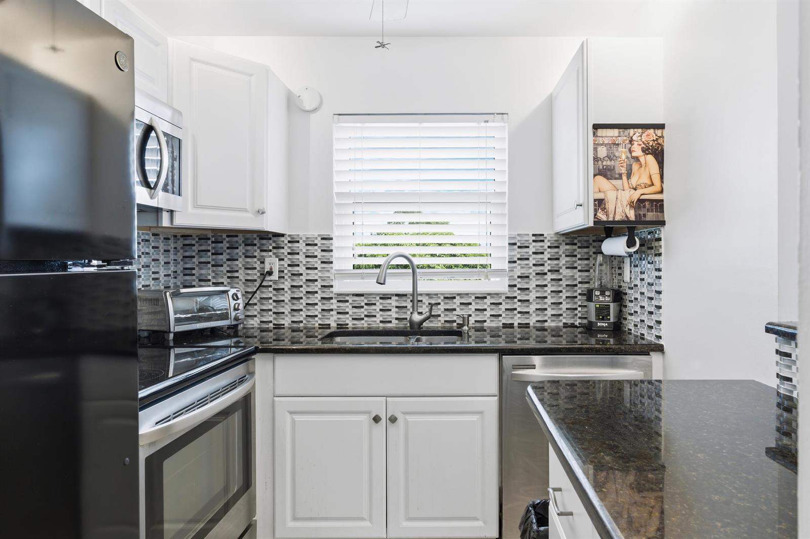 A kitchen features white cabinets, dark granite countertops, a mosaic tile backsplash, and stainless appliances — 70 Bedford # C, West Palm Beach FL 33417, WEST PALM BEACH, FL