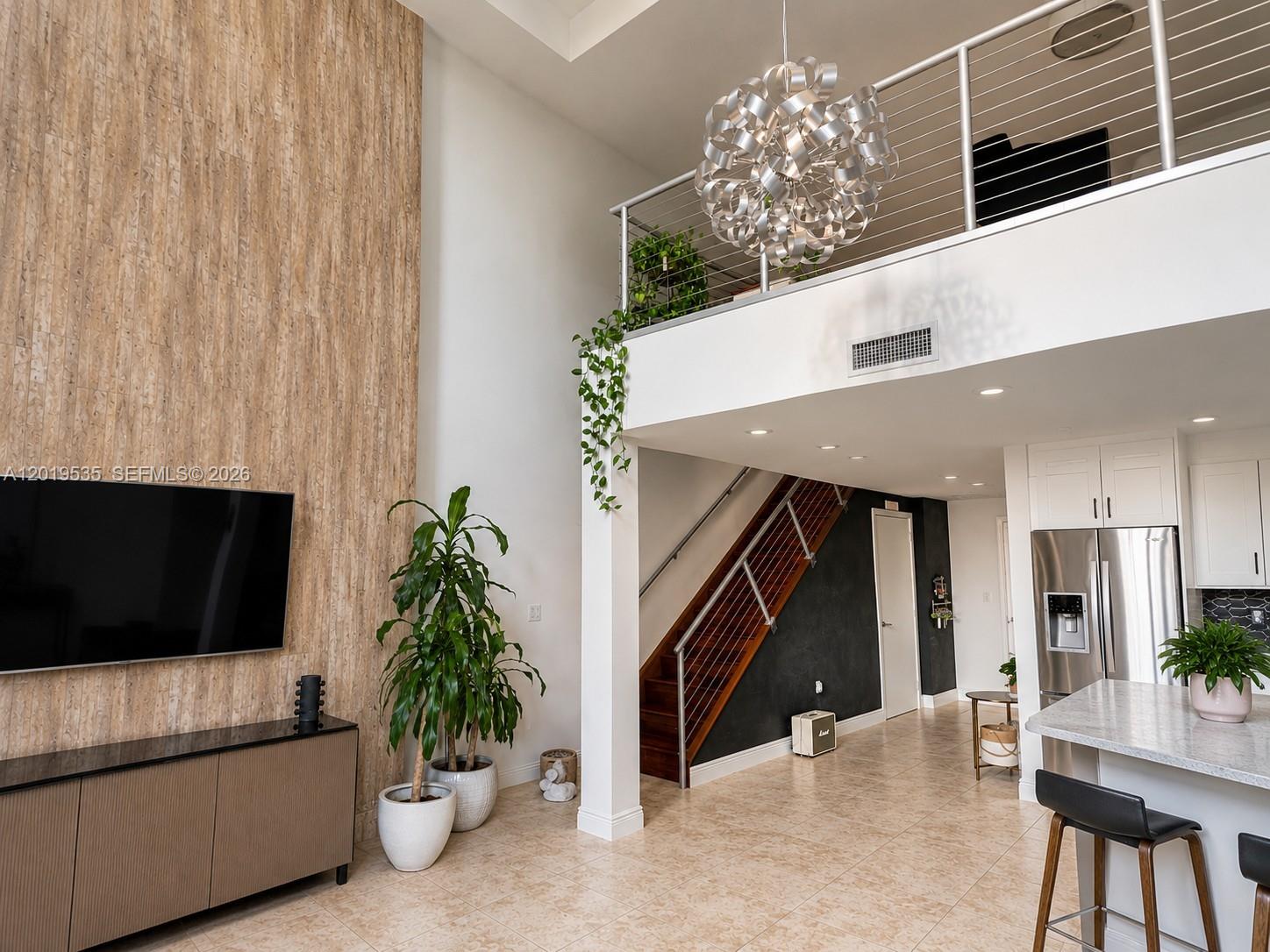 A modern living room features a tall wood-paneled wall, a staircase, and a lofted area — 1050 Brickell Ave # 410, Miami FL 33131, MIAMI, FL