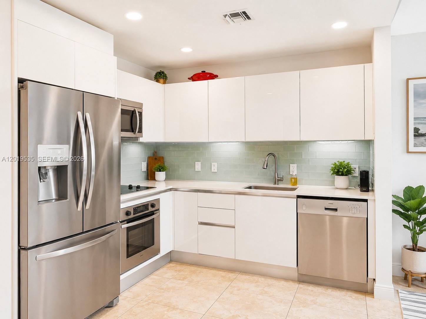 A modern kitchen features white cabinets, stainless steel appliances, and a light green tile backsplash — 1050 Brickell Ave # 410, Miami FL 33131, MIAMI, FL