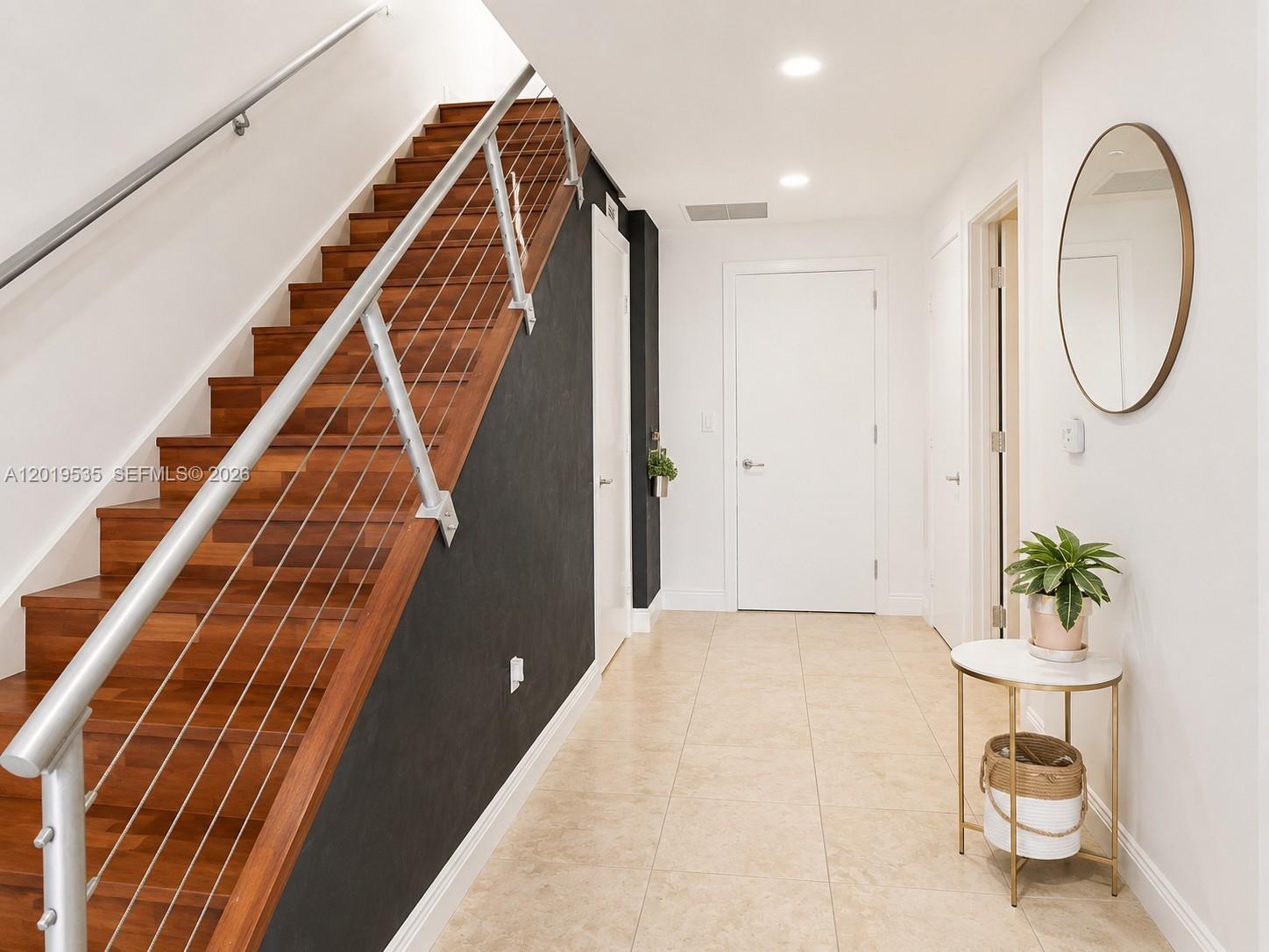 A hallway features a wooden staircase with a cable railing, tiled floors, and white doors — 1050 Brickell Ave # 410, Miami FL 33131, MIAMI, FL