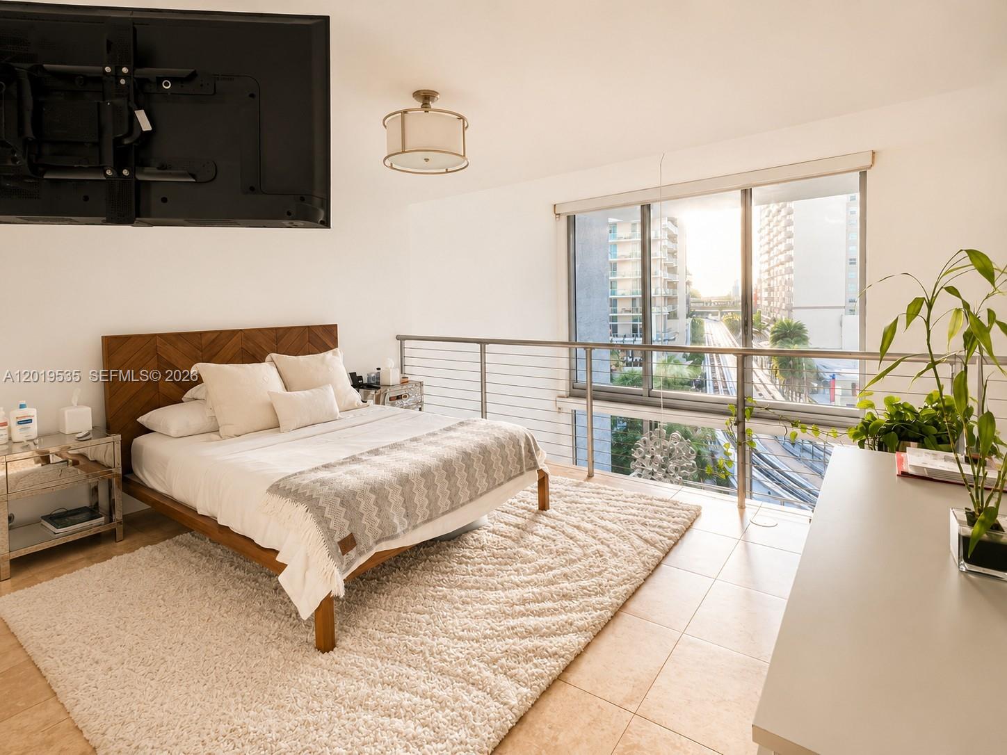 A bedroom features a wooden bed, a large rug, and a balcony overlooking a city street — 1050 Brickell Ave # 410, Miami FL 33131, MIAMI, FL