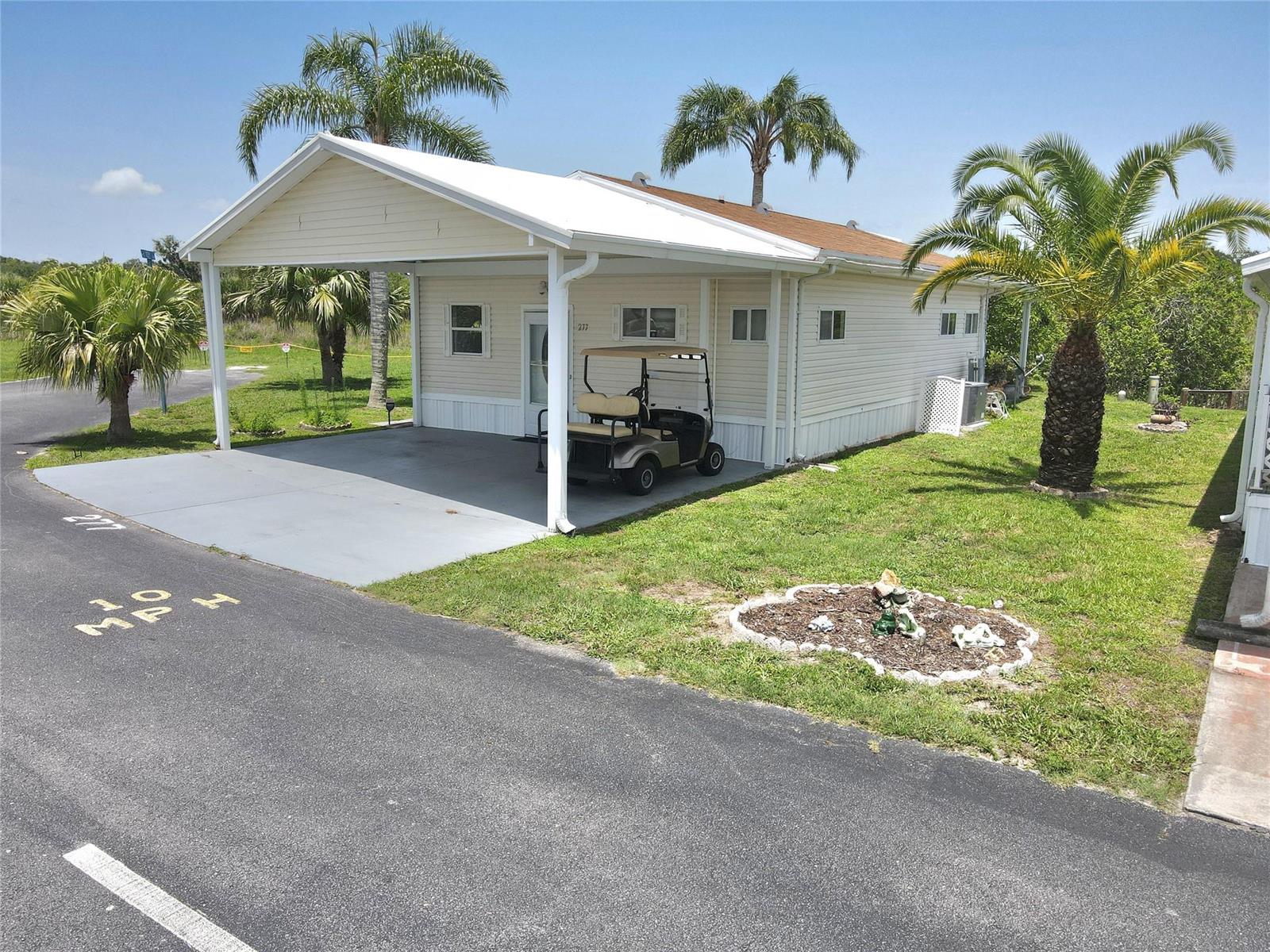 A light-colored mobile home features a covered carport, a golf cart, and palm trees — 12310 SE 143rd Avenue, FL 34974, FL