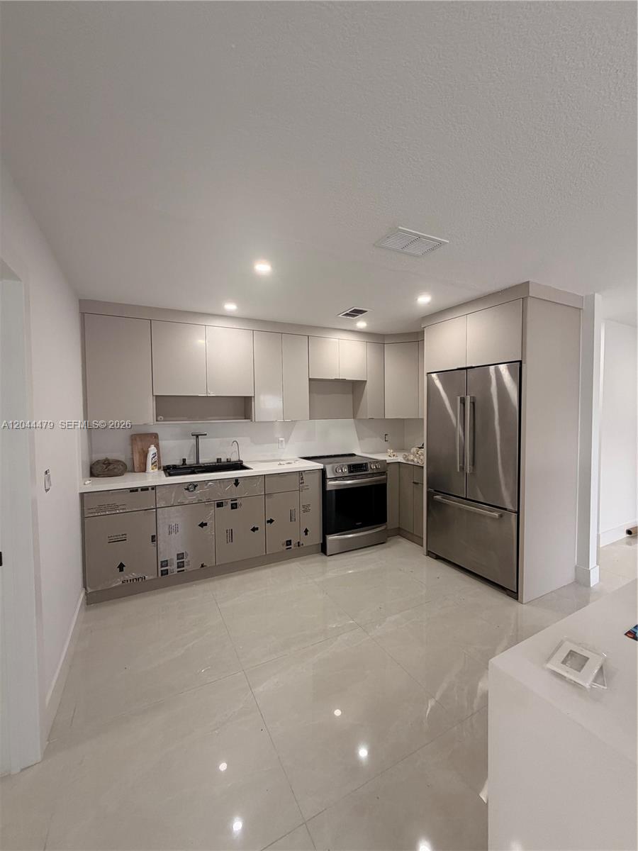 A modern kitchen features light-colored cabinetry, stainless steel appliances, and large, glossy floor tiles — 191 SE 6th Ave, Hialeah FL 33010, HIALEAH, FL