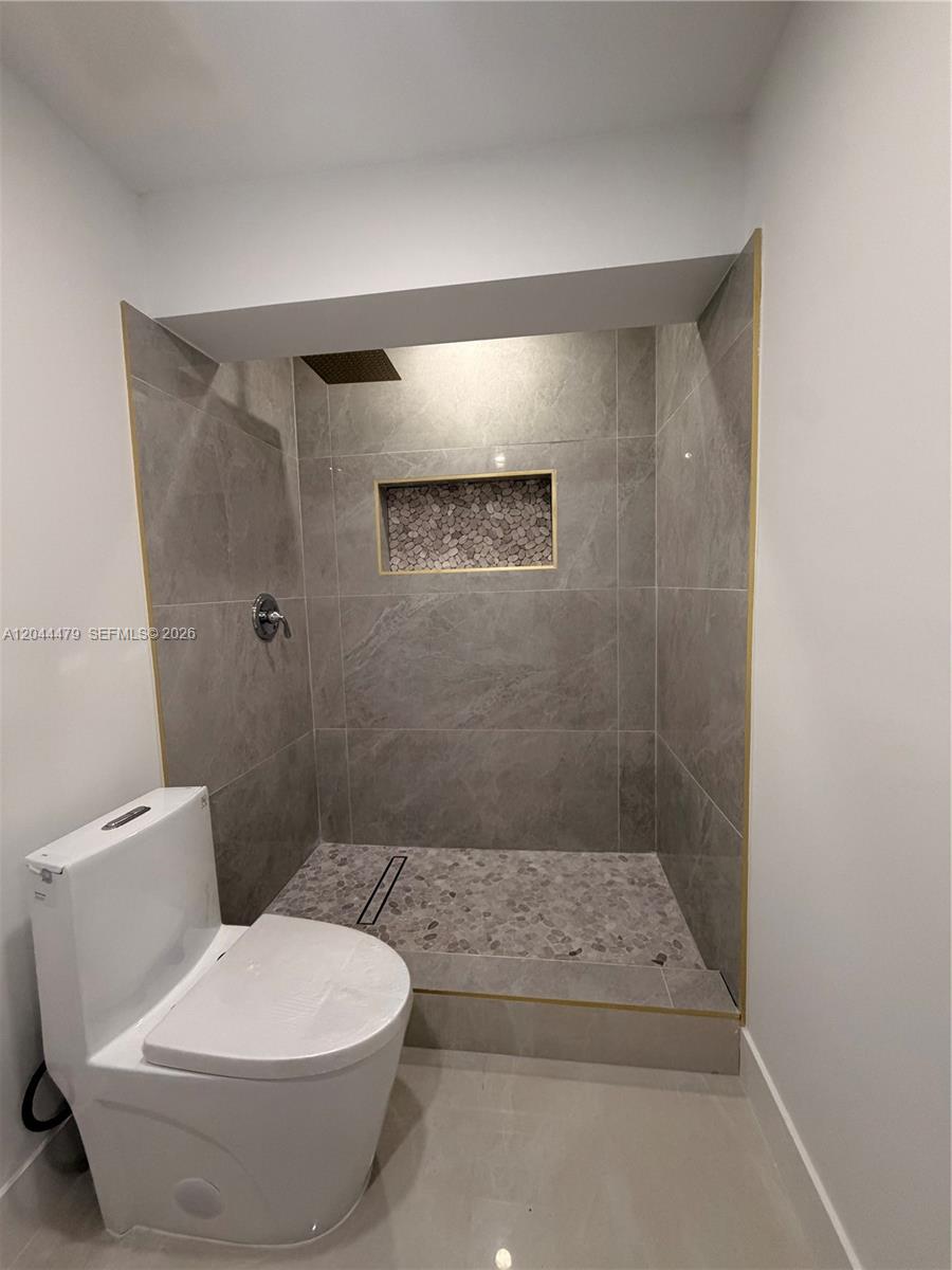A bathroom features a toilet next to a walk-in shower with gray tile and pebbles — 191 SE 6th Ave, Hialeah FL 33010, HIALEAH, FL