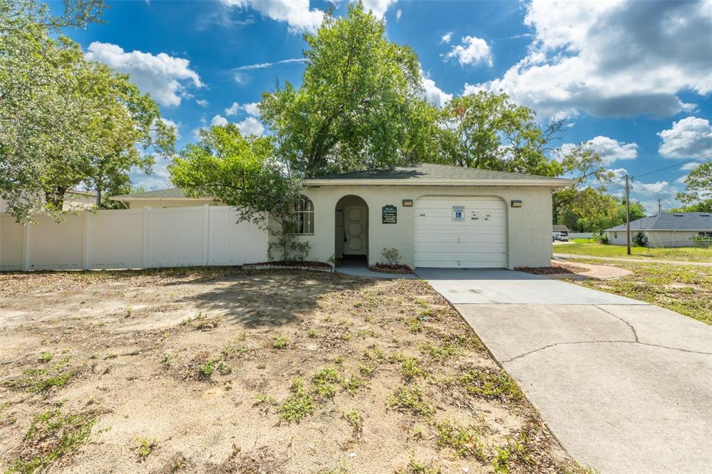 A single-story house with a white garage door, arched entryway, and a white privacy fence — 1492 MARINER BOULEVARD, SPRING HILL, FL
