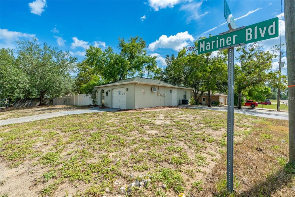 A single-story house with a garage and a street sign stands on a grassy lot — 1492 MARINER BOULEVARD, SPRING HILL, FL