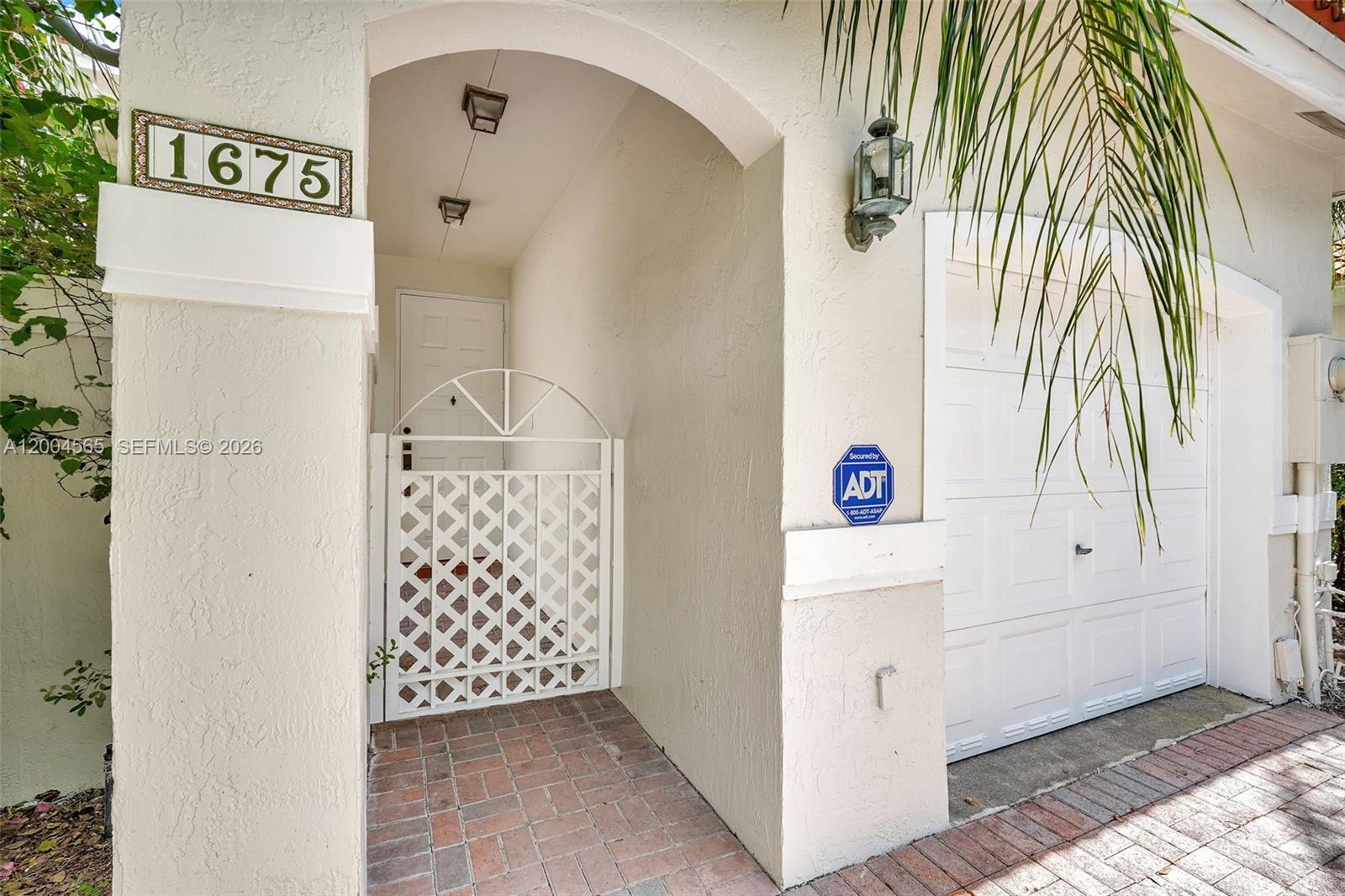 The exterior view shows a house entrance with a white gate, brick walkway, and garage — 1675 Yellowheart Way, Hollywood FL 33019, HOLLYWOOD, FL
