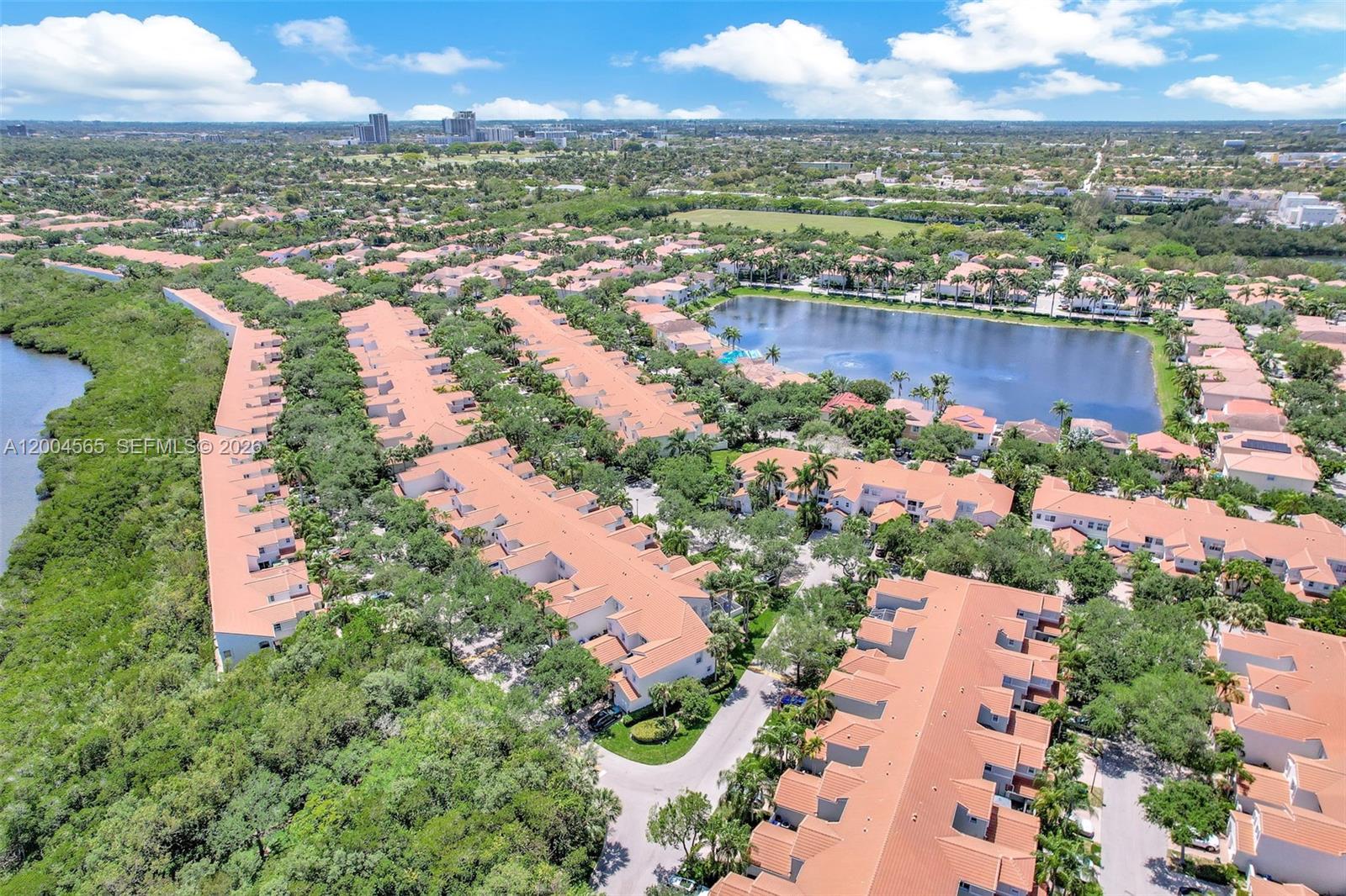 An aerial view shows a residential complex with terracotta-roofed townhomes surrounding a central lake — 1675 Yellowheart Way, Hollywood FL 33019, HOLLYWOOD, FL
