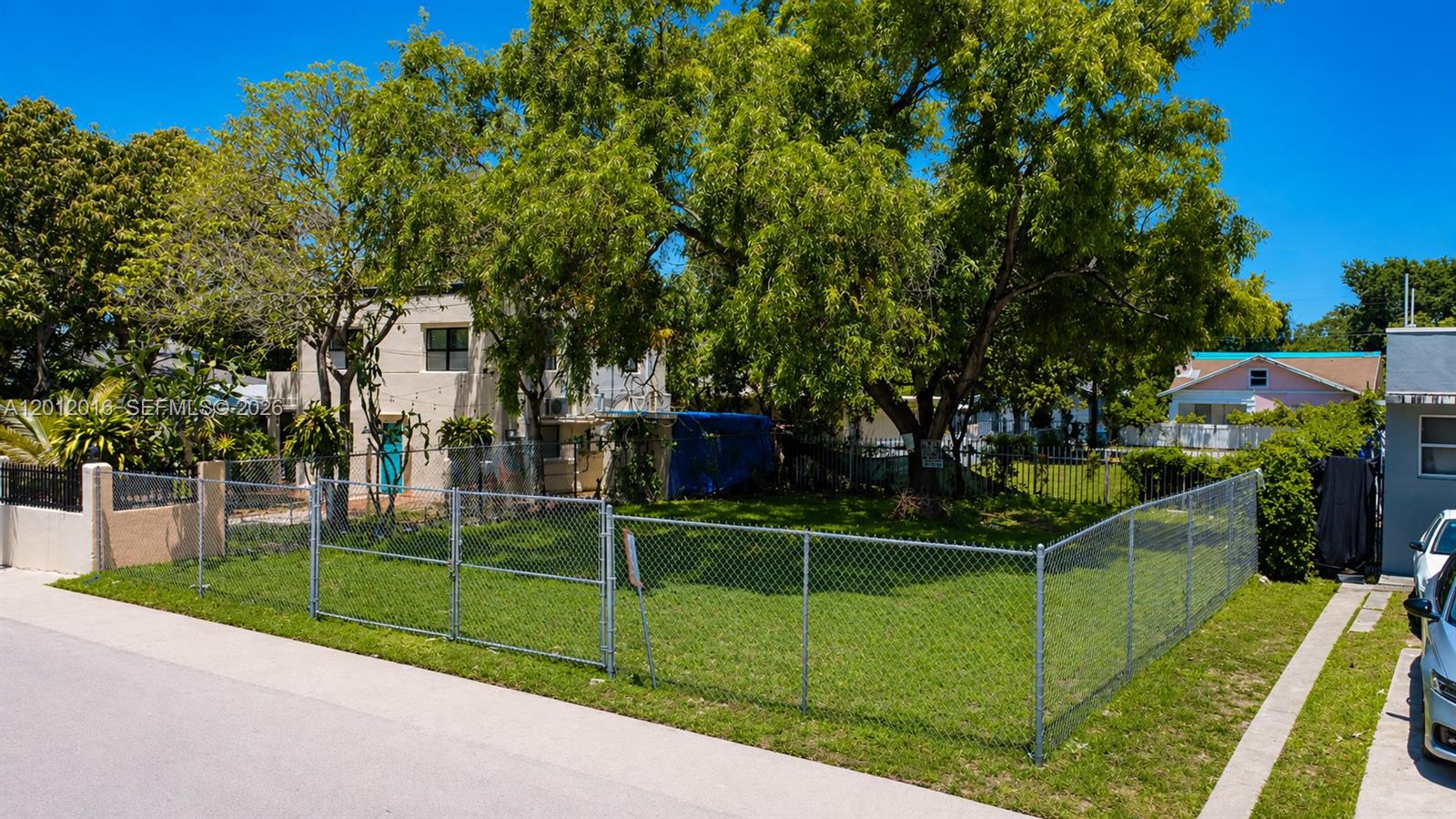 A fenced, grassy vacant lot sits next to a two-story building and a large tree — 285 NE 55th St, Miami FL 33137, MIAMI, FL