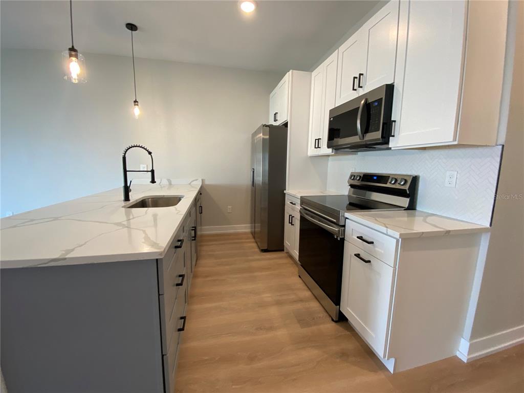 A kitchen features white cabinets, stainless steel appliances, and a gray island with a sink — 10524 PENDLETON AVENUE, ENGLEWOOD, FL
