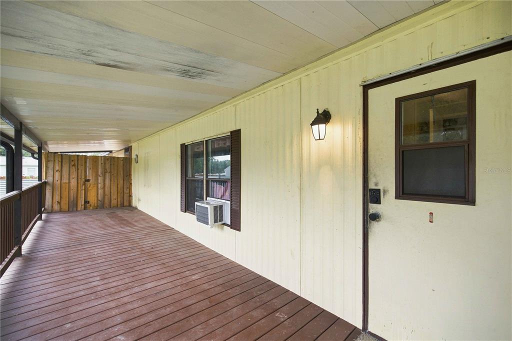 A covered wooden porch features a light-colored exterior wall, a window with an air conditioner, and a door — 12313 SE 86TH AVENUE, BELLEVIEW, FL
