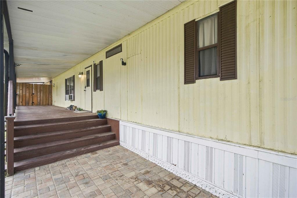 A covered wooden deck with stairs leads to the entrance of a yellow mobile home — 12313 SE 86TH AVENUE, BELLEVIEW, FL