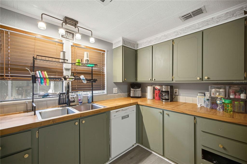A kitchen features sage green cabinets, wood countertops, a double sink, and a white dishwasher — 12313 SE 86TH AVENUE, BELLEVIEW, FL