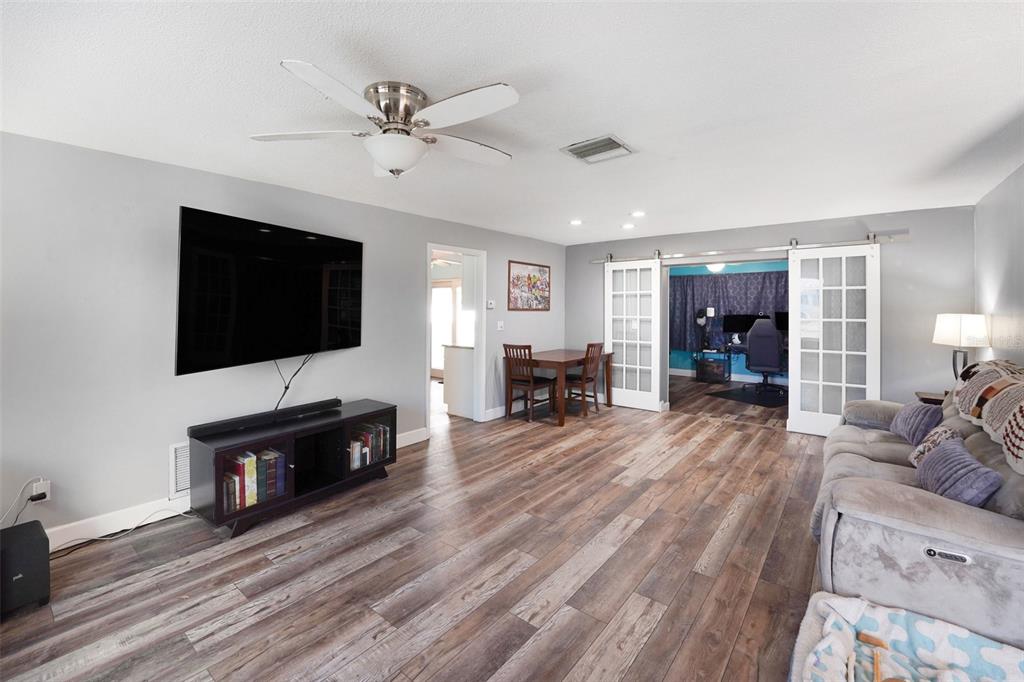 A living room with wood-look flooring, a wall-mounted television, and sliding glass doors to an office — 2561 BLACKWOOD CIRCLE, CLEARWATER, FL