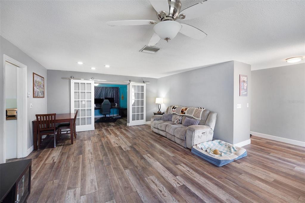 A living room with wood-look flooring, a gray sofa, and sliding glass doors to an office — 2561 BLACKWOOD CIRCLE, CLEARWATER, FL