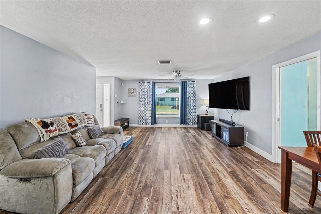 A living room with wood-look flooring, a gray sofa, and a wall-mounted television — 2561 BLACKWOOD CIRCLE, CLEARWATER, FL