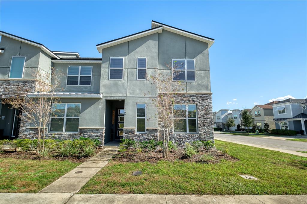 A two-story townhouse exterior features gray stucco walls, stone veneer accents, and a front walkway — 1700 TROPICAL PALMS CIRCLE, KISSIMMEE, FL
