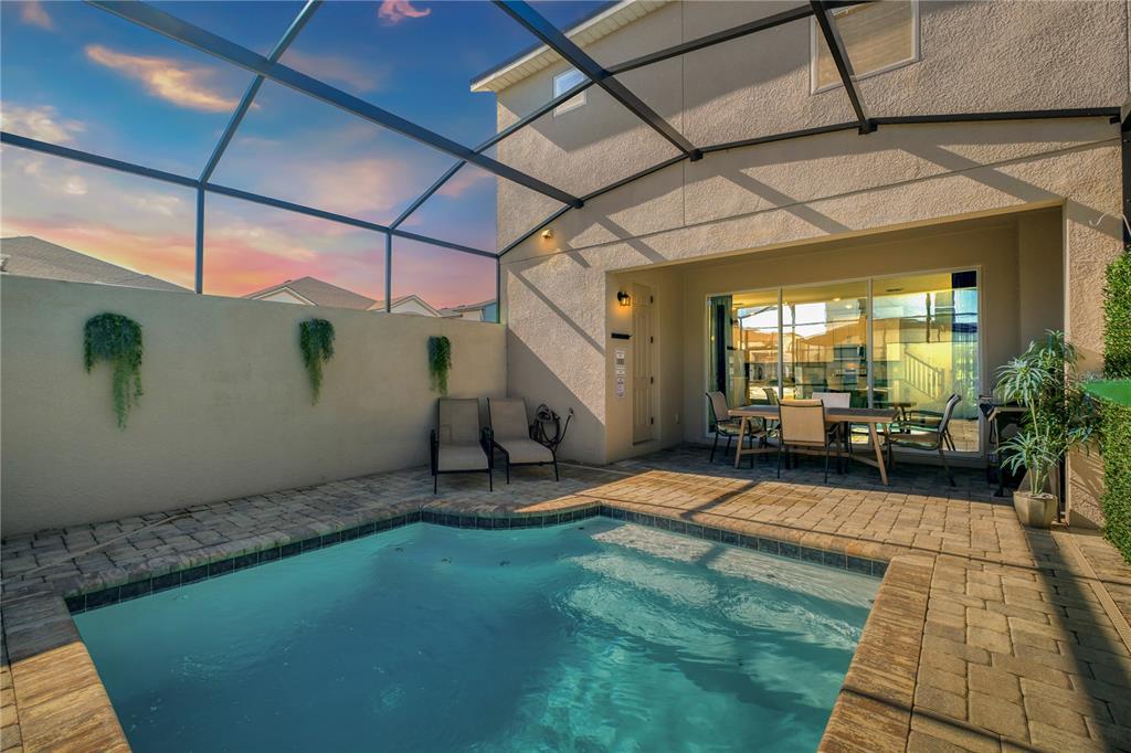 A screened-in patio features a small swimming pool, paver decking, and outdoor dining furniture — 1700 TROPICAL PALMS CIRCLE, KISSIMMEE, FL