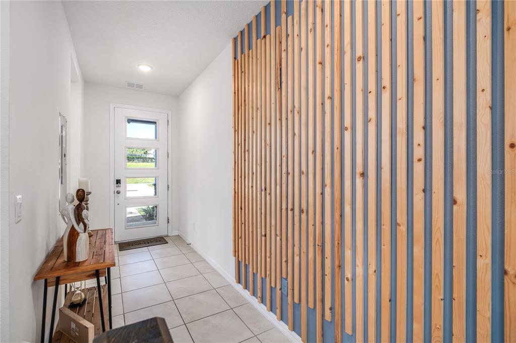 An entryway features a light-colored tile floor, a white front door, and a wood-slat accent wall — 1700 TROPICAL PALMS CIRCLE, KISSIMMEE, FL