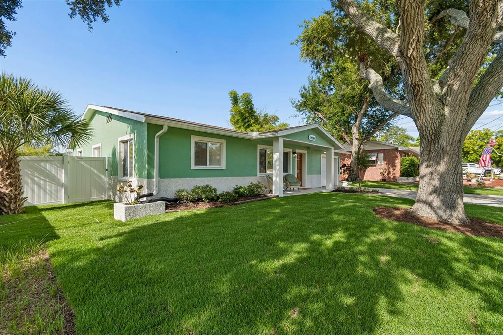 A green single-story house with a white fence, a large tree, and a grassy lawn — 14584 APACHE AVENUE, LARGO, FL