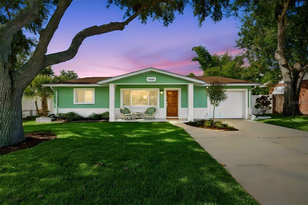 A single-story green house with a white garage, a front porch, and a grassy lawn — 14584 APACHE AVENUE, LARGO, FL