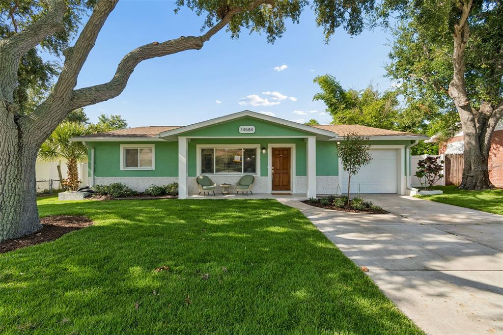 A single-story green house with a white garage and a front lawn with trees — 14584 APACHE AVENUE, LARGO, FL