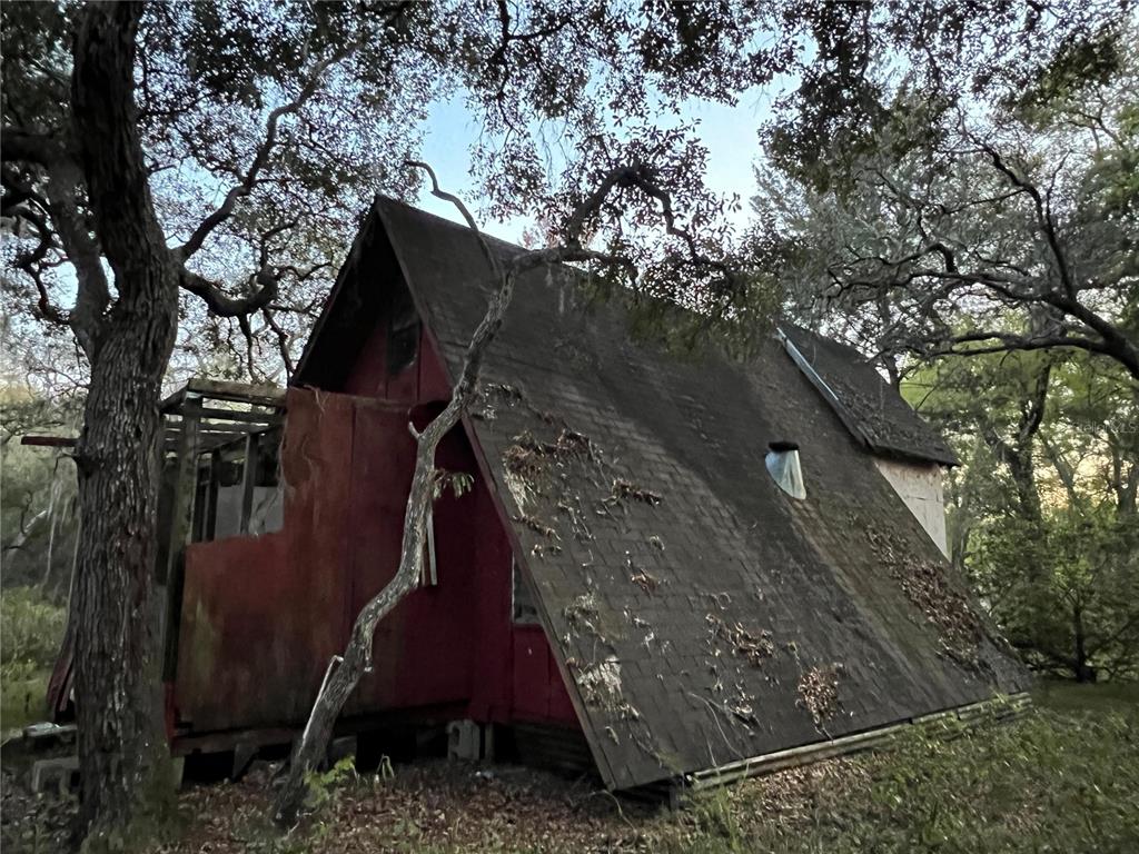 A weathered, red A-frame cabin sits nestled among trees in a wooded area — 19435 SE 92ND PLACE, OCKLAWAHA, FL