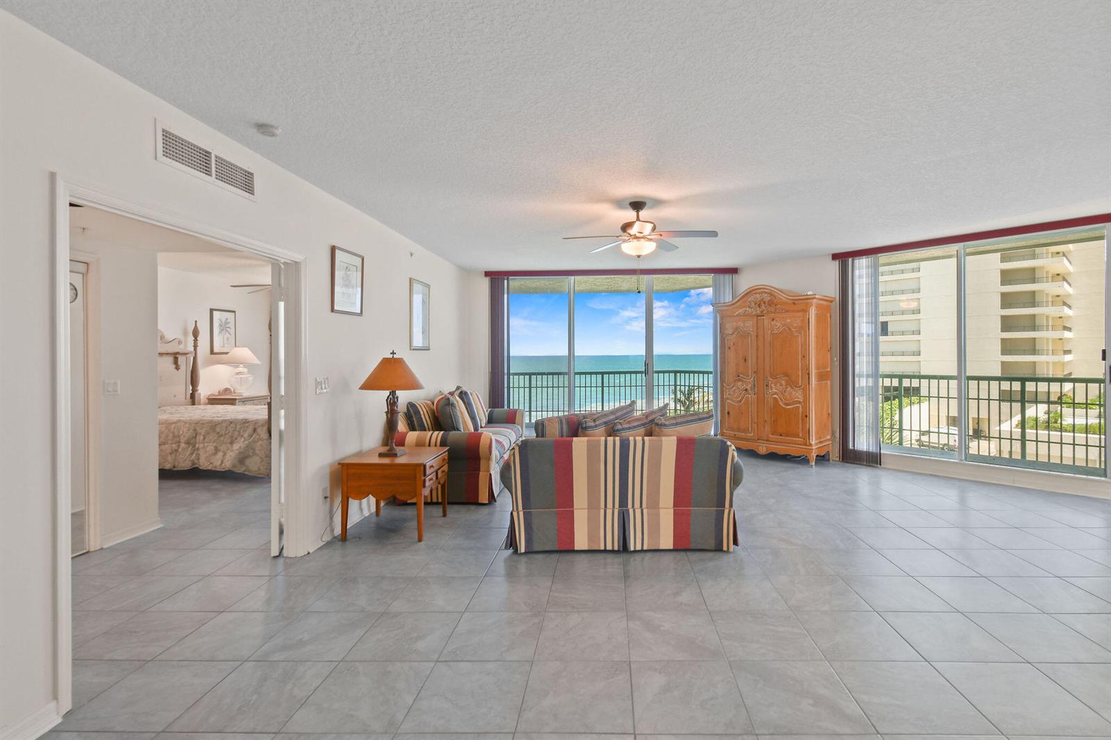 A living room with striped furniture, tile floors, and a balcony overlooking the ocean — 8650 S Ocean Drive # 306, Jensen Beach FL 34957, JENSEN BEACH, FL